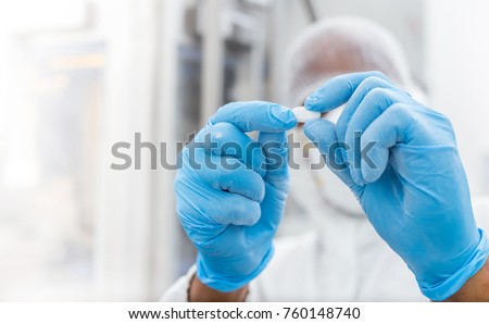Pharmaceutical worker examining pill. Pharmaceutical manufacturing inspection of a pill or tablet. Drug tablet being inspected. Medicine pill being checked for quality.
