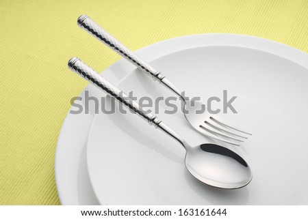 Dinnerware, spoon and fork with plates on the yellow table