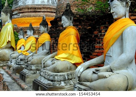 Ayutthaya, Thailand:  A row of stone Buddhas adorned with orange and yellow silk sashes in the cloister gallery near two brick chedis at Wat  Yai Chai Mongkhon