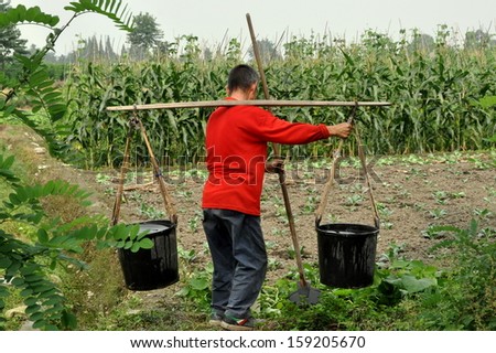 PENGZHOU, CHINA:  Farmer carrying two plastic pails filled with water using a shoulder yoke