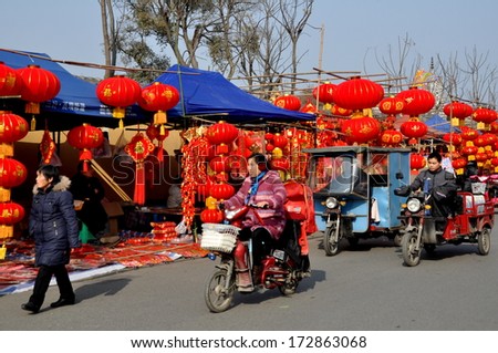 Pengzhou, China January 22, 2014:  Bright red lanterns and other Chinese New Year decorations sold by vendors line the street in front of the Long Xing Monastery