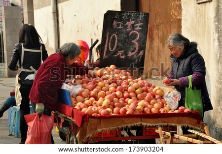 Pengzhou, China January 28, 2014:  Elderly women selling apples from her bicycle cart filled with the fruits
