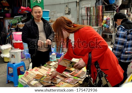 PENGZHOU, CHINA JAN 29, 2014:  Fashionably dressed Chinese woman shopping for chopsticks from a vendor at the Long Xing outdoor marketplace