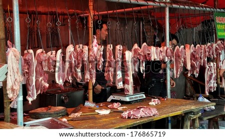 Pengzhou, China - April 10, 2011:  Slabs of pork hang from iron meat hooks at a butcher shop in the Long Xing marketplace