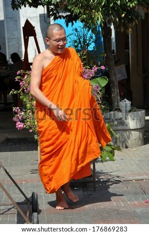 Bangkok, Thailand - December 17, 2011:  Buddhist monk in traditional orange robe walking bare-footed in a garden at Wat Hua Lamphong
