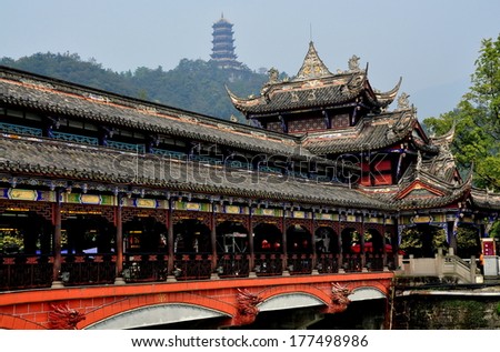 Dujiangyan, China - October 9, 2013:  The Ming Dynasty Nan Qiao covered bridge over the Min River with distant hilltop pagoda