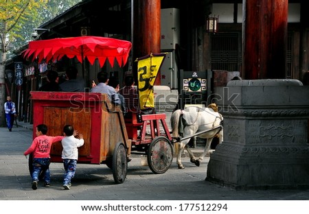 Langzhong Ancient City, China:  Two little Chinese boys walking behind a wooden horse-drawn tourist carriage pretend to help push it along the old stone streets