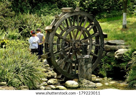 CHENGDU, CHINA - APRIL 24, 2005:  Two little boys walk past  a wooden water wheel at the Du Fu Thatched Cottage historic site
