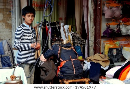 JIU CHI TOWN, CHINA - December 1, 2007:  Chinese teen waiting for a clothing repair at a local tailor shop where woman works at her sewing machine