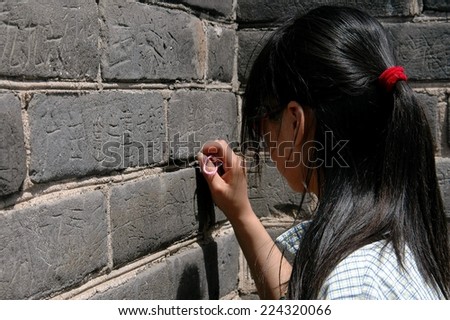 Badaling, China - May 1, 2005:  A young Chinese woman uses a key to carve her name into one of the stone blocks of the Great Wall of China