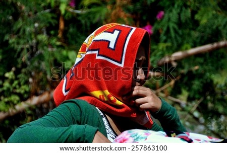Hua Hin, Thailand - January 1, 2010:  Thai woman riding in a pickup truck shields her face from the sun using a towel as a head scarf