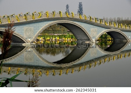 Qingbaijiang, China - October 30, 2012:  A graceful Chinese bridge with three arches festooned with cascading yellow Mums is reflected in the water at Phoenix Lake Park\'s 2012 Chrysanthemum Exposition