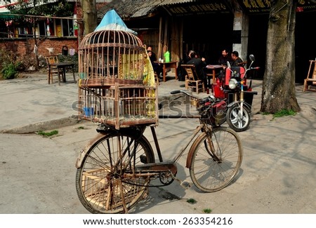 Long Feng, China - March 5, 2013:   Bicycle with two wooden bird cages strapped on the back parked near a group of men seated at outdoor tables playing cards