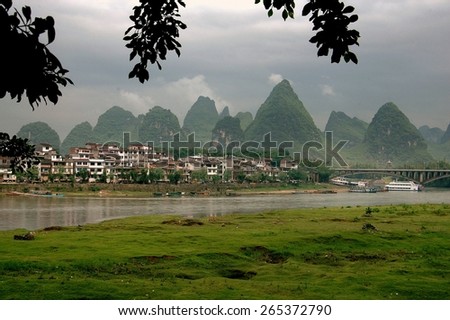 Yangshuo, China - April 29, 2007:  Dramatic karst rock formations covered with trees rise above riverside houses on the banks of the Lijiang River