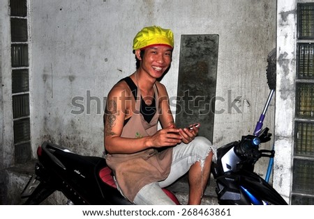 Bangkok, Thailand - January 22, 2013:  Smiling Thai man with arm tattoos sitting on his motorcycle with his cell phone