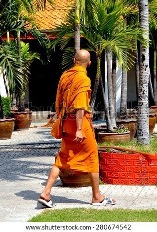 Bangkok, Thailand - January 19, 2011:  Buddhist monk in orange robe walking in the gardens dotted with palm trees at Wat Mahathat