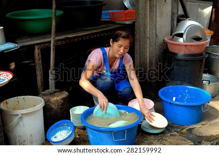 Bangkok, Thailand - December 20, 2005: Thai woman washing dishes in blue plastic pots outdoors at a Chinatown restaurant