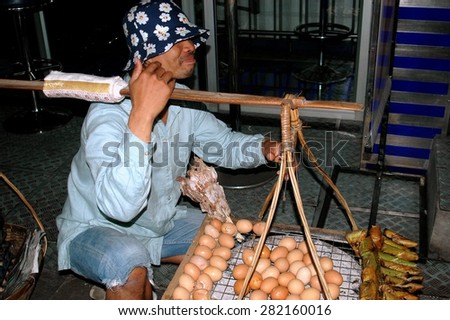 Bangkok, Thailand - December 27, 2005:  Thai vendor sitting on a Sukhamvit Road sidewalk selling fresh eggs carried in a shoulder yoke basket