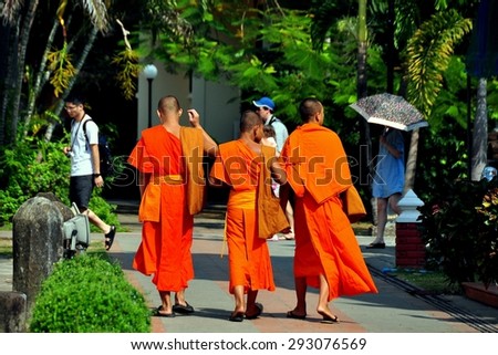 Chiang Mai, Thailand - January 3, 2013:  Three youthful Buddhists monks wearing bright orange robes walking in the gardens at Wat Phra Singh  *