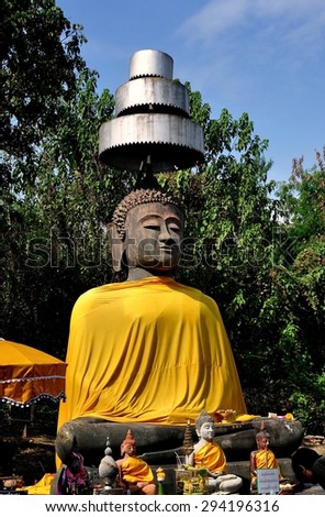 Chiang Mai, Thailand - December 30, 2012: A large stone Buddha draped in an orange silk robe and covered by a three-tiered metal parasol at Wat That Khao at Wiang Kum Kam Ancient Village