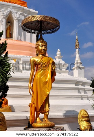 Chiang Mai, Thailand - December 30, 2012:  Standing gilded statue of Buddha shaded by a metal parasol in front of the great white Wat Changkam chedi at Wiang Kum Kam Ancient Village