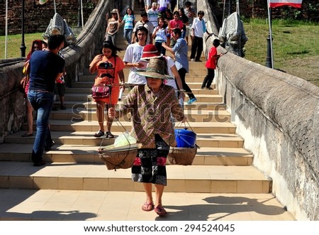 Lampang, Thailand - December 28, 2012: Thai woman carrying two straw baskets suspended from a shoulder yoke on the entrance stairway to Wat Phra That Lampang Luan