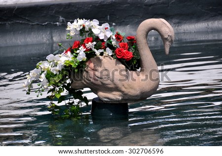 Newport, Rbode Island - July 17, 2015:  A carved swan planter with white orchids and red roses stands in a water basin in the gardens at 1898-1902 Rosecliff mansion
