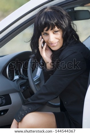 A pretty young caucasian white business woman getting out of her nice car. She has a call on her smartphone while looking straight into the camera.