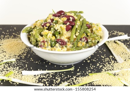 A closeup image of dinner plate with vegan couscous salad on red and green beans. Image taken on white background with garnish of dry couscous corn and veggies.