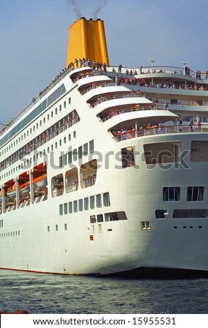 Closeup of a large cruise ship while leaving the harbor with a lot of passengers on the deck