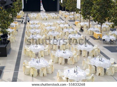 Large dining table set for wedding, dinner or another corporate event with beautiful decoration between green trees inside with people moving blurred