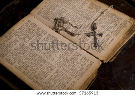 Open pages of an ancient holy bible with a silver cross lying on it, image taken over dark old background