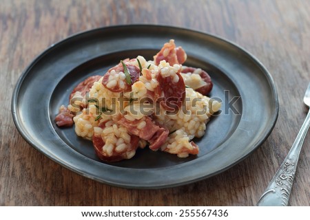 Risotto with sausage, cured ham and rosemary on a tin plate.