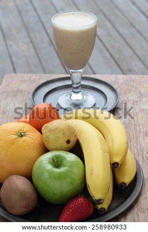 Glass full of banana milk smoothie on a tin plate.
