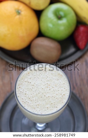 Glass full of banana milk smoothie on a tin plate.