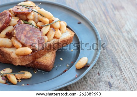 Toast with beans and chorizo cooked with rosemary leaves on a tin plate.
