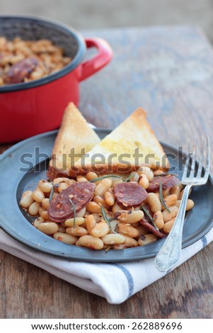 Beans and chorizo cooked with rosemary leaves on a tin plate.