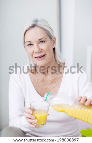 Senior woman pouring herself a glass of orange juice.