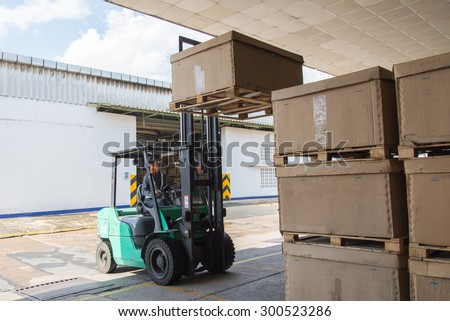 Warehouse worker driver in uniform stacking cardboxes by forklift stacker loader