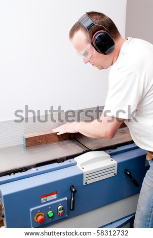 Carpenter working on an electric buzz saw cutting some boards, he is wearing safety glasses and hearing protection to make things safe