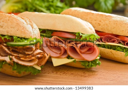 Three fresh sandwiches - turkey breast, ham & swiss and salami on a cutting board. Focus on the ham sandwich