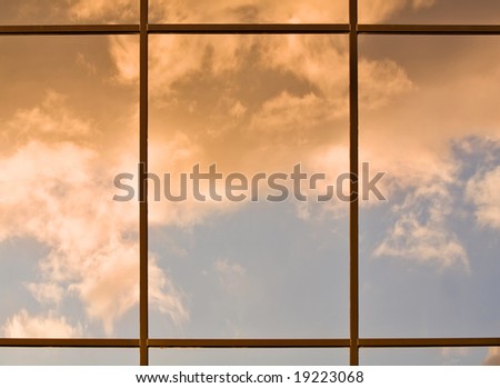 Clouds lit by the setting sun reflecting in a modern office building windows
