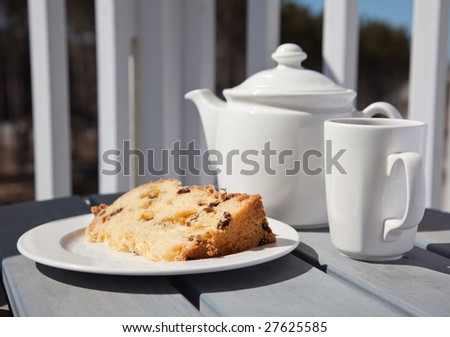 A cup of tea and a slice of fruit cake served on a balcony