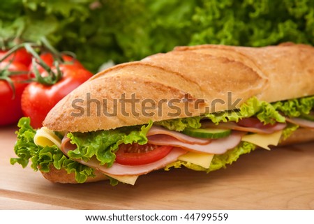 Large submarine sandwich with ham, swiss cheese, lettuce and tomatos on a wooden cutting board