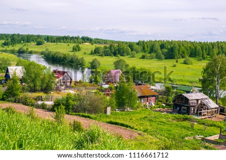 Russian rural landscape in summer, village houses on the river bank in greenery