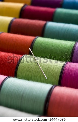 various colours of cotton reels in a row with a needle