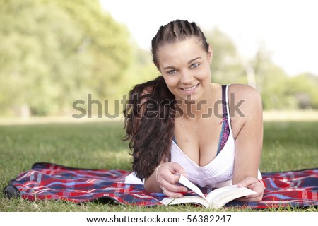 young attractive girl lying on picnic rug while reading a book