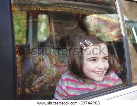 girl smiling and looking out of car window at fairground ride with reflection of carousel in glass