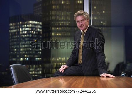 Business man sitting on table in boardroom looking at camera