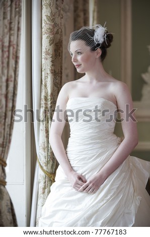 Pretty bride looking out of window and smiling on her wedding day